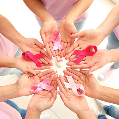 Hands placed in a circle, holding various pink and red ribbons.